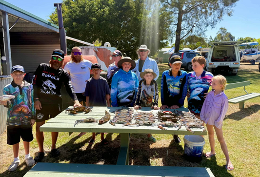 Adults and children gathered around a picnic table displaying fish and crabs at the Flathead & Crab Classic.