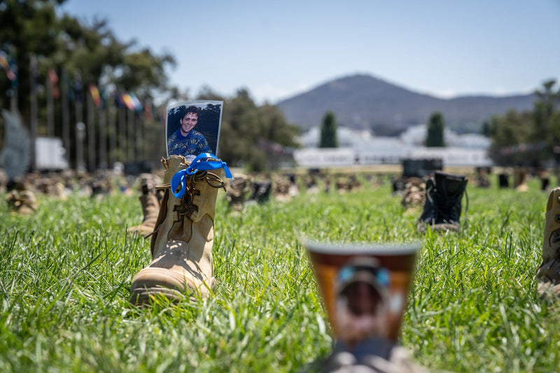 A boot with a blue ribbon and a photograph at the Canberra remembrance display, with Parliament House behind it.