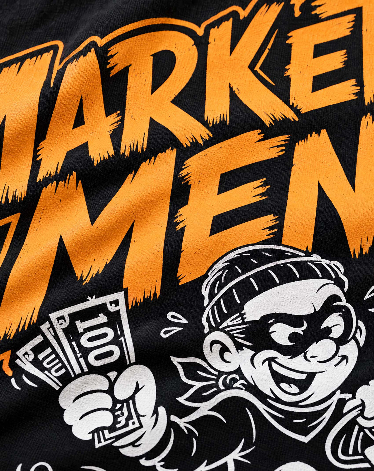 Close-up of the Marketplace Menace Tee print: orange lettering and a cartoon bandit holding a fistful of cash